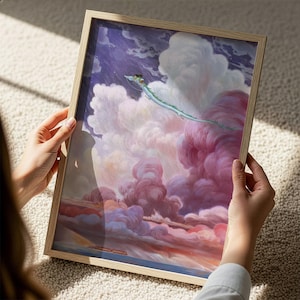 A person is holding a framed painting depicting a fantastical scene with a dragon-like creature soaring through a vibrant, cloud-filled sky.
