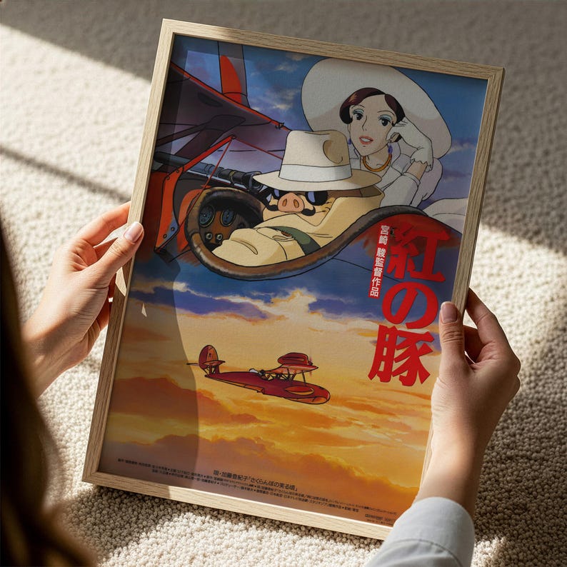 A person is holding a framed poster featuring an animated scene with a woman in a white hat and a red airplane flying in the sky.