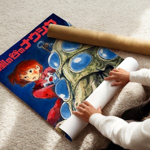 A person is holding a roll of paper and a poster featuring an illustration of a character, likely from a children's book or anime.