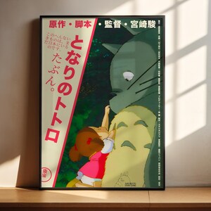 The image is a framed poster featuring an illustration of a young girl interacting with a large, green creature, possibly a cat or a dragon. The poster has Japanese text on it, which appears to be related to the story or characters depicted in the illustration.