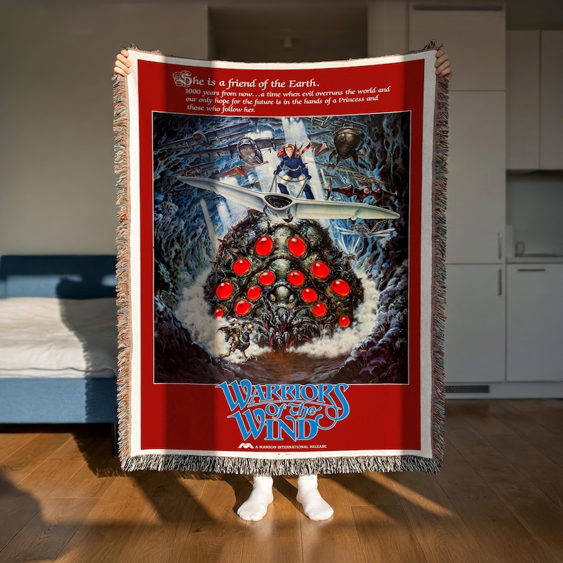 A person is holding up a large poster or artwork featuring a fantastical scene with a large creature, red objects, and a spaceship. The poster has a red background with white text and graphics.