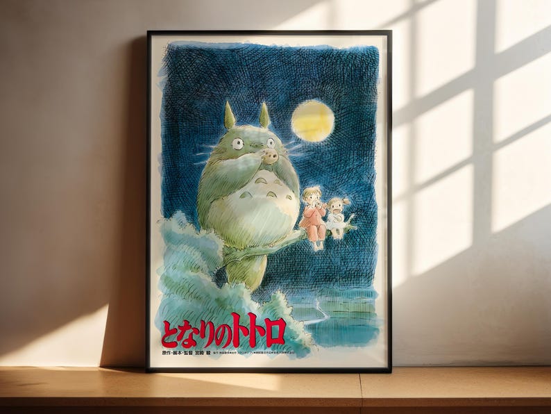 The image is a framed poster featuring a whimsical illustration of a large, green creature with horns and a yellow moon in the background, accompanied by two smaller figures.