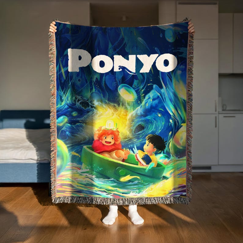 A person is holding up a colorful blanket with the word "PONYO" printed on it, which features an illustration of two characters in a boat on a wave.