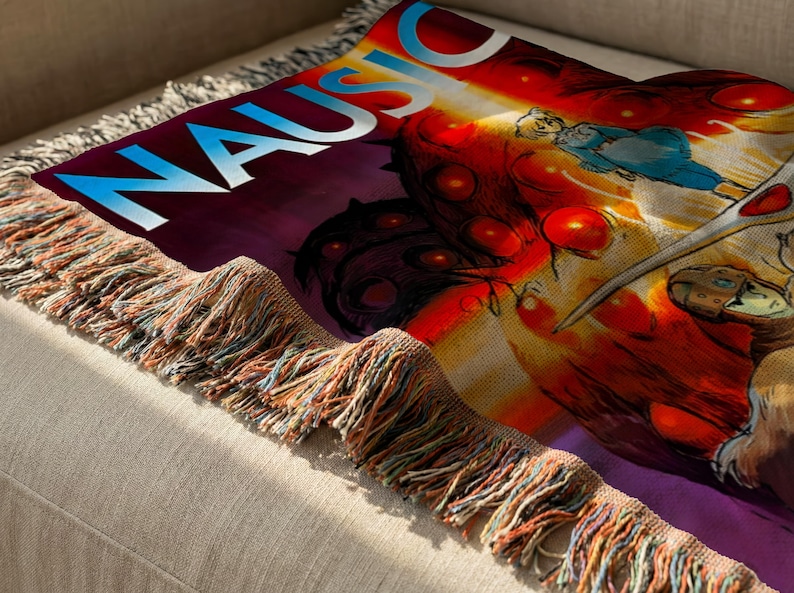 a colorful, abstract design with a mix of red, orange, and purple colors, along with various shapes and patterns. The design appears to be a textile or fabric item, possibly a blanket or throw, with a fringe or fringe-like texture.