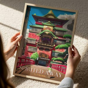 A person is holding a framed poster of the castle of Spirited Away from the Studio Ghibli film.