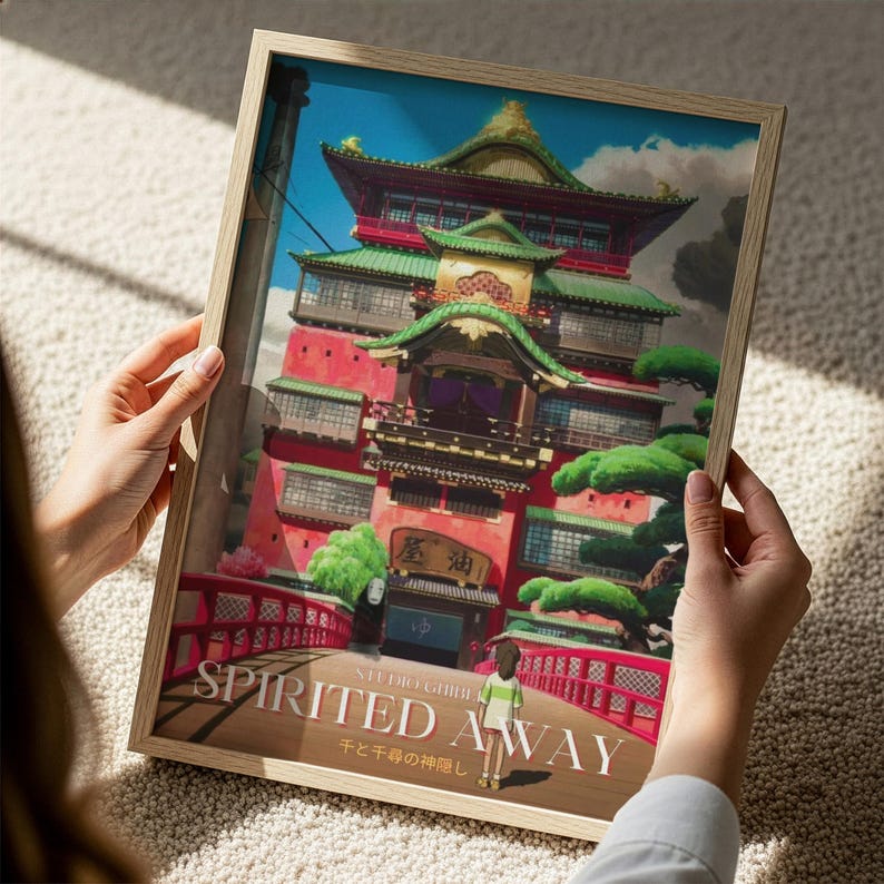A person is holding a framed poster of the castle of Spirited Away from the Studio Ghibli film.