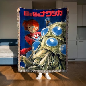 A person is holding up a large blanket with an illustration of a character from a Japanese animated film.