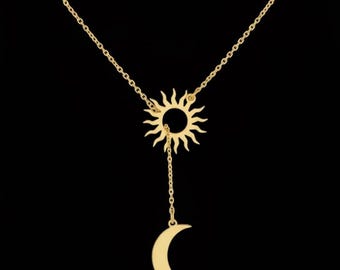 May include: Gold-colored necklace featuring a sun pendant with a dangling crescent moon. The sun pendant has a detailed design with rays, and the moon is a smooth, curved shape. The necklace is on a black background.