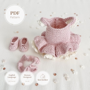 May include: A crochet pattern PDF for a dusty pink dress with a ruffled skirt, matching booties, and a hair accessory. The dress features a cream-coloured ruffled hem. Text on the image includes PDF Pattern, English Language (US Terms), Human Designed, and KreAtelier.