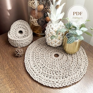 May include: A beige crocheted placemat with a central hole, alongside matching coasters. A decorative pineapple and a small potted plant are also visible. The image includes the text "PDF Pattern".