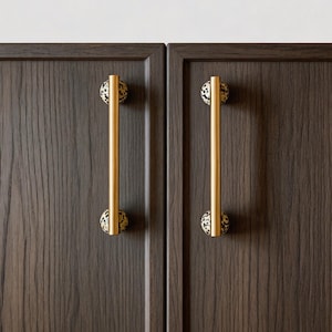 Puede incluir: Primer plano de dos puertas de armario de madera oscura con tiradores dorados. Los tiradores son cilíndricos con una esfera moteada negra y beige en cada extremo. Las puertas del armario tienen un patrón de vetas de madera vertical.