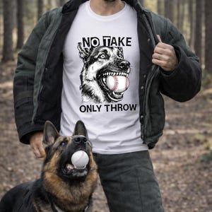 Może przedstawiać: Biała koszulka z grafiką owczarka niemieckiego trzymającego piłkę do baseballu w pysku oraz napisem "NO TAKE ONLY THROW". Owczarek niemiecki również trzyma piłkę do baseballu. Koszulka jest noszona przez osobę.