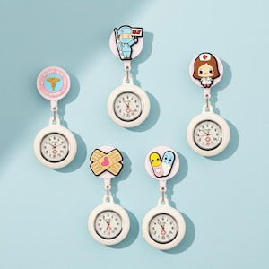 May include: A collection of white nurse fob watches, each with a different cartoon-style topper. The toppers include a nurse, a medical cross, and a bandage. The watches have a round face with black numbers and red hands. One reads "PROUD TO BE A NURSE".