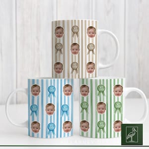 Puede incluir: Tres tazas de cerámica blanca con diferentes patrones de rayas: beige, azul y verde. Cada taza presenta un patrón repetido de la cara de un bebé y una cinta "#1 Papá". Las tazas están diseñadas para el Día del Padre o un nuevo papá.