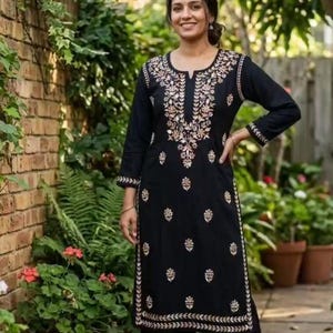 May include: A black long-sleeved tunic and matching wide-leg trousers set featuring a round neckline with a small slit. The garment is decorated with intricate gold-toned floral embroidery along the neckline, cuffs, and hemline.