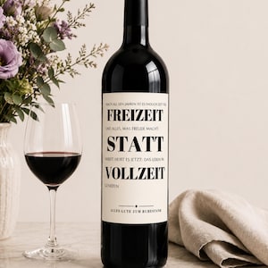 May include: A dark glass wine bottle with a cream-colored label featuring black text that reads: NACH ALL DEN JAHREN IST ES ENDLICH ZEIT FÜR FREIZEIT UND ALLES, WAS FREUDE MACHT. ARBEIT HEIBT ES JETZT: DAS LEBEN IN VOLLZEIT GENIEBEN ALLES GUTE ZUM RUHESTAND.