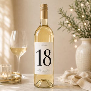 Op de afbeelding: Een heldere glazen wijnfles met een gouden schroefdop en een wit rechthoekig etiket. Het etiket bevat het woord CHAPTER bovenaan, het grote zwarte cijfer 18 in het midden en de tekst Cheers to your NEXT ADVENTURE aan de onderkant.