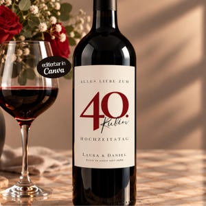 Könnte beinhalten: Eine dunkle Weinflasche mit einem cremefarbenen Etikett, das den Text ALLES LIEBE ZUM 40. HOCHZEITSTAG, die Namen LAURA & DANIEL sowie den Satz HAND IN HAND SEIT 1986 trägt. Ein mit Rotwein gefülltes Weinglas steht neben der Flasche.