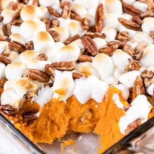 May include: A close-up shot of a sweet potato casserole in a glass baking dish. The casserole is topped with toasted marshmallows and pecans. The sweet potato filling is a vibrant orange color.