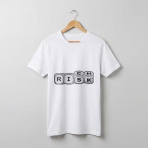 May include: White t-shirt with the word "RICH" spelled out using keyboard keys. The word "RISK" is visible, with the letters arranged in a row. The shirt is hanging on a wooden hanger against a plain background.