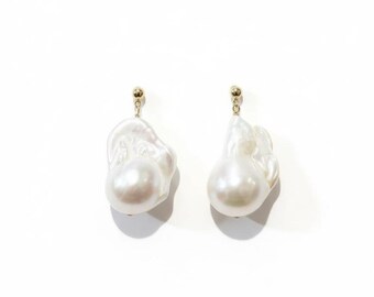 May include: A pair of white baroque pearl earrings with gold-colored posts. The pearls have an irregular, organic shape and a lustrous surface, set against a white background. The earrings are a classic jewelry item.