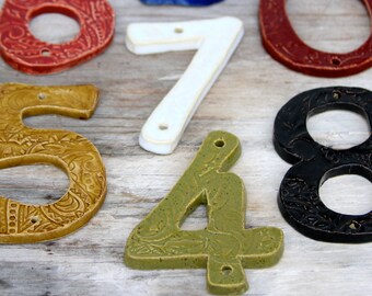 May include: A set of ceramic house numbers in various colors and patterns. The numbers include 0, 4, 5, 6, 7, and 8. The numbers are all hand-painted and have a rustic, vintage look.