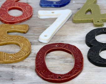 May include: A set of ceramic house numbers in various colours and styles. The numbers include 0, 3, 4, 5, 6, 7, and 8. Some of the numbers have a patterned design.