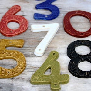May include: A set of ceramic house numbers in various colors and patterns. The numbers include 0, 4, 5, 6, 7, and 8. The numbers are all hand-painted and have a rustic, vintage look.