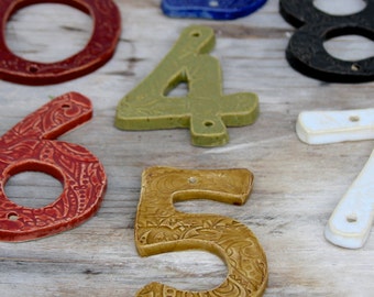Może przedstawiać: Zestaw ceramicznych numerów domowych w różnych kolorach i stylach. Numery to 0, 4, 5, 6, 7, 8 i 3. Numery są ręcznie malowane i mają unikalny, rustykalny wygląd.