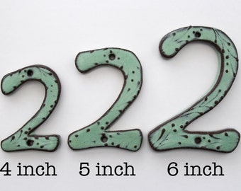 May include: Three ceramic house number signs in the shape of the digit 2, featuring a light green glaze with dark brown speckled edges and detailing. The numbers are labelled with text indicating heights of 10.16 cm, 12.7 cm, and 15.24 cm.
