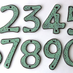 May include: Ten ceramic house numbers, 1 through 10, in a light green color with brown accents. The numbers are hand-painted with a speckled design.