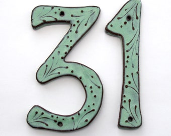 May include: A pair of ceramic house numbers, 31, in a light green color with brown accents. The numbers have a rustic, hand-painted look.