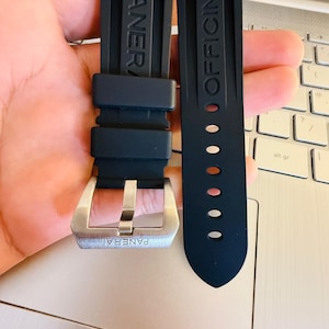 May include: Black rubber watch strap with the brand name "PANERAI" embossed on one strap and "OFFICINE" on the other. The strap features a silver-colored buckle.