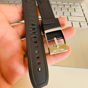 Puede incluir: Correa de reloj de goma negra con el nombre de la marca "BREITLING" en relieve. La correa presenta una hebilla plateada con el logotipo de Breitling. La correa est&aacute; dise&ntilde;ada para un reloj.