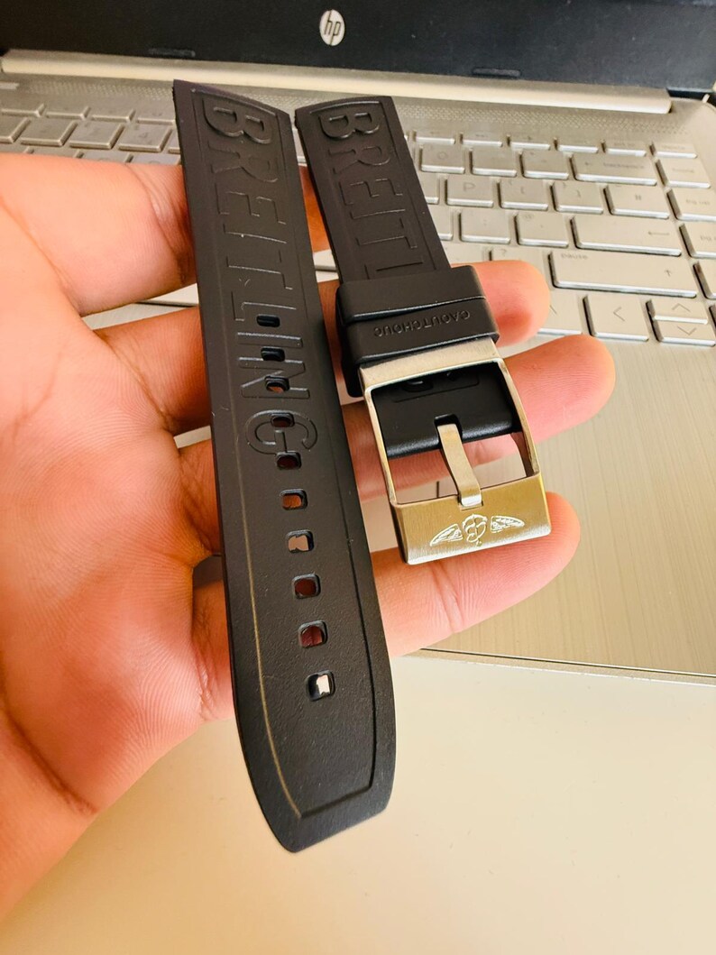 Puede incluir: Correa de reloj de goma negra con el nombre de la marca "BREITLING" en relieve. La correa presenta una hebilla plateada con el logotipo de Breitling. La correa est&aacute; dise&ntilde;ada para un reloj.