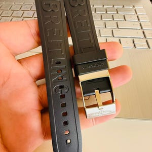 Puede incluir: Dos correas de reloj negras con la palabra "BREITLING" en relieve. Una correa tiene una hebilla plateada. Las correas est&aacute;n hechas de un material flexible y est&aacute;n dise&ntilde;adas para un reloj.
