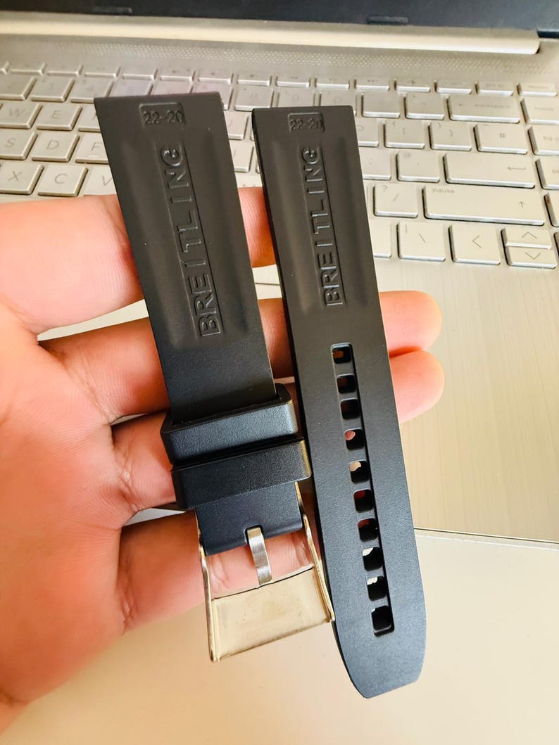 Puede incluir: Dos correas de reloj Breitling negras. Una correa tiene una hebilla plateada y la otra tiene orificios de ajuste. Las correas est&aacute;n marcadas con el logotipo de Breitling y el tama&ntilde;o 22-20 o 22-21.