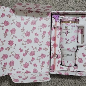 Puede incluir: Una taza de cer&aacute;mica blanca con asa negra y el texto "But First, Coffee" en negrita negra. La taza se encuentra sobre un fondo borroso, sugiriendo un ambiente acogedor.