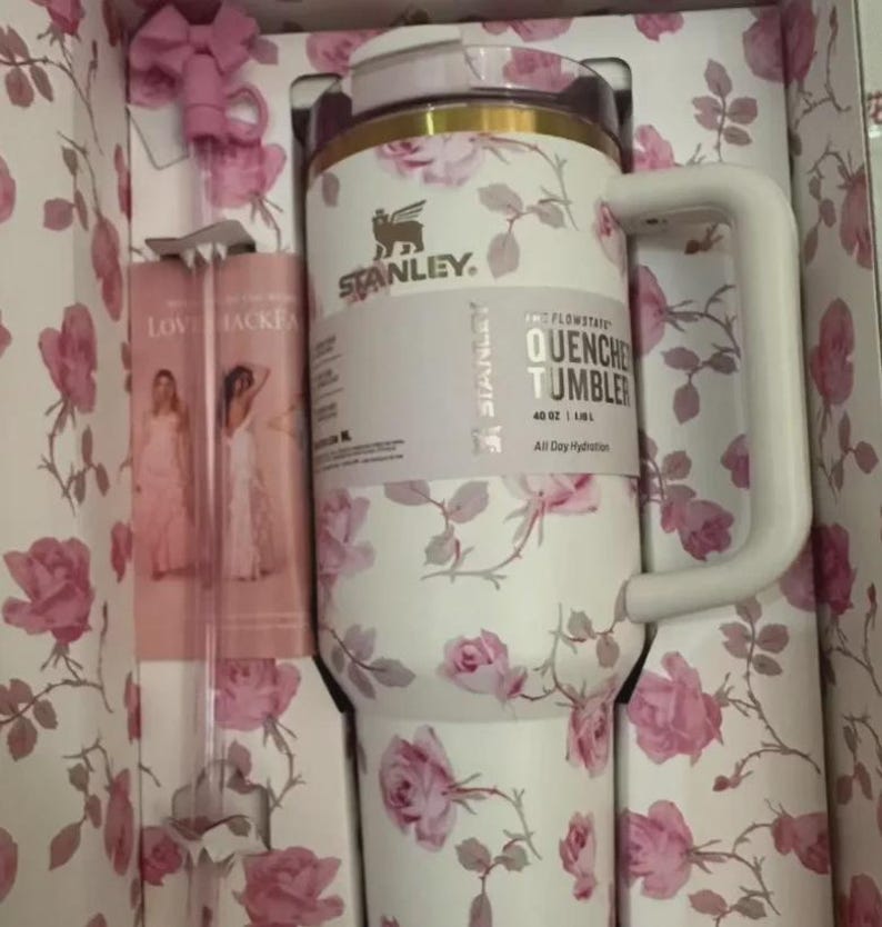 Puede incluir: Un vaso Stanley Quencher blanco con un estampado floral de rosas, un asa blanca y una tapa rosa. El vaso est&aacute; en una caja con un dise&ntilde;o floral a juego e incluye una pajita rosa. El texto en el vaso dice "QUENCHER TUMBLER 1.18L".