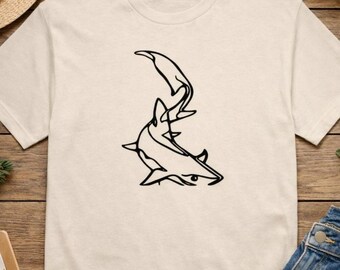 Puede incluir: Camiseta color crema con un dibujo lineal negro de un tiburón. El diseño del tiburón está estilizado y parece estar nadando hacia arriba. La camiseta es de un material suave y tiene cuello redondo.