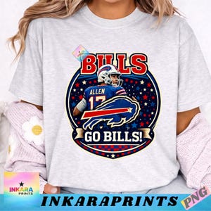 Puede incluir: Camiseta gris claro con un gráfico de un jugador de fútbol americano con uniforme azul y blanco. El diseño incluye el texto "BILLS" en rojo y blanco, el nombre del jugador "ALLEN" y el número "17", y la frase "GO BILLS!"