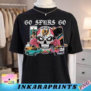May include: Black t-shirt with the text "GO SPURS GO" above a colorful sugar skull design. The design includes roses, cars, and a candle. The shirt also features the text "INKARAPRINTS" at the bottom.