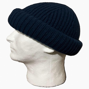 May include: A dark navy blue beanie cap featuring a thick ribbed knit texture and a wide, folded cuff. The hat is constructed with a rounded crown and a snug fit, showcasing a consistent vertical ribbed pattern throughout the entire garment.