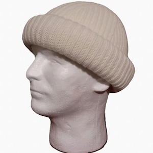 May include: A solid white beanie hat featuring a thick, ribbed knit texture and a wide, folded cuff. The hat is displayed on a white, featureless mannequin head, highlighting the clean, uniform color and the structured, circular design.
