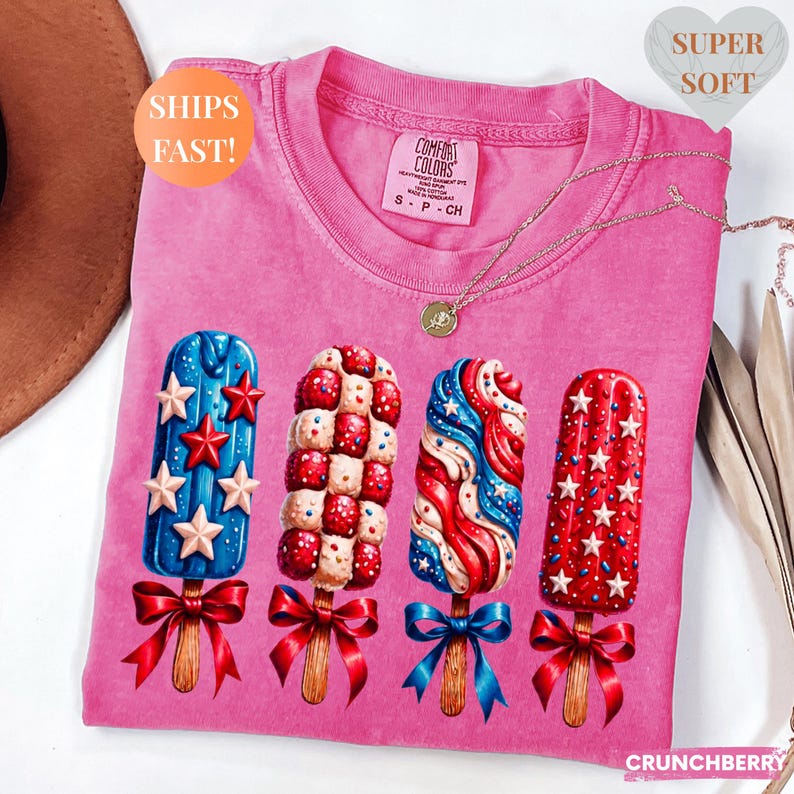 Pu&ograve; includere: T-shirt rosa Comfort Colors con quattro disegni di ghiaccioli rossi, bianchi e blu con fiocchi. La maglietta ha il testo "SHIPS FAST!" e "SUPER SOFT" sopra. Una collana d'oro &egrave; drappeggiata sulla maglietta.