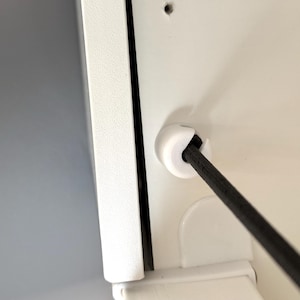 Könnte beinhalten: Nahaufnahme eines weißen Schranks mit einem schwarzen Kabel, das durch eine weiße Kunststofftülle verläuft. Der Schrank hat ein sauberes, modernes Design mit glatter, glänzender Oberfläche. Das Kabel ist abgewinkelt.