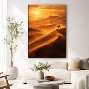 May include: A rectangular wall art print featuring a desert landscape at sunset with golden orange hues. The scene depicts a lone camel and rider silhouetted against the bright sun atop a large, sweeping sand dune with visible windblown sand.