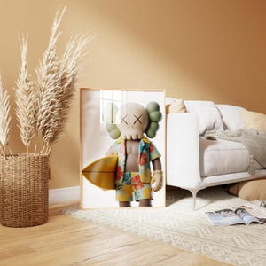 May include: Framed artwork featuring a cartoon figure with a skull-like face, wearing a Hawaiian shirt and shorts, holding a yellow surfboard. The figure has green hair and beige gloves. The artwork is displayed in a light wood frame.