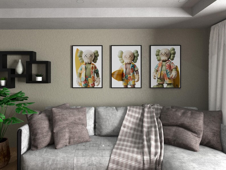 May include: Three framed art prints featuring a cartoon figure with X-shaped eyes and a floral shirt, holding a surfboard. The prints are displayed above a gray sofa with throw pillows and a plaid blanket. A decorative wall shelf and a potted plant are also visible.