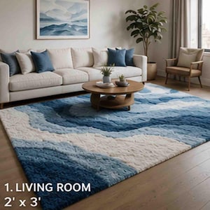 May include: A blue and white area rug with a wave-like pattern, measuring 2 feet by 3 feet, is displayed in a living room setting. The rug's design incorporates shades of blue and white, creating a textured, ocean-inspired aesthetic. The room includes a white sofa and a wooden coffee table.